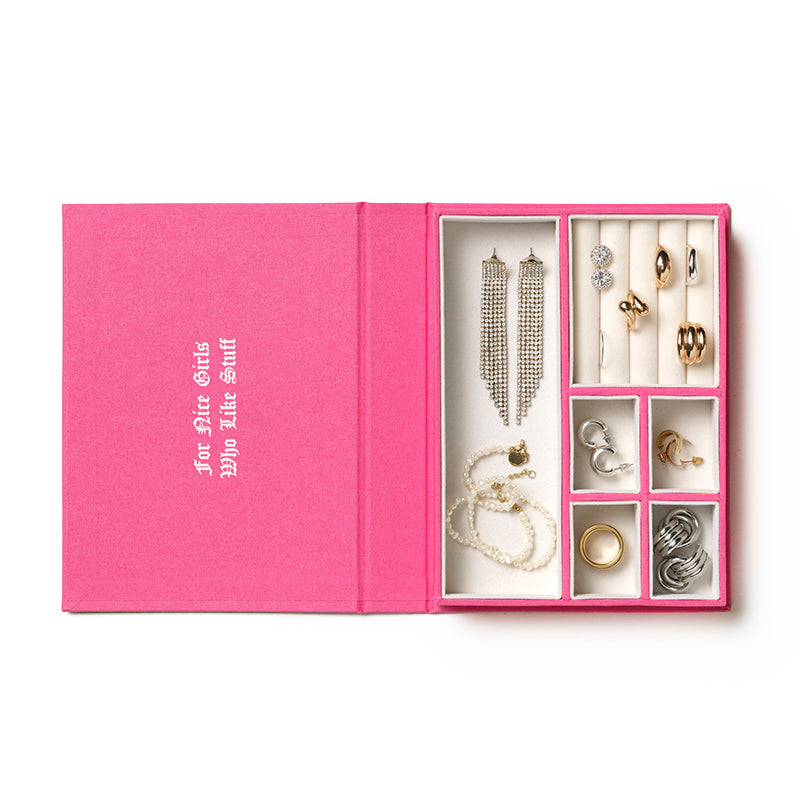 An open Juicy Couture x Printworks Jewelry Box in pink displays a neatly organized collection of earrings, rings, and bracelets. The lid features the phrase “For the Girls Who Like Stuff” in white text, making this charming book-inspired jewelry box perfect for showcasing your favorite accessories.