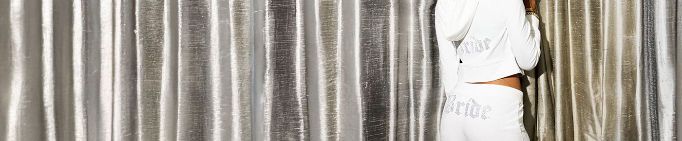 Person wearing a white tracksuit with "Bride" against a metallic curtain