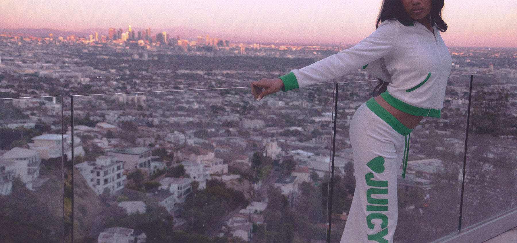 Person wearing a white tracksuit with green accents, standing in front of a cityscape view.