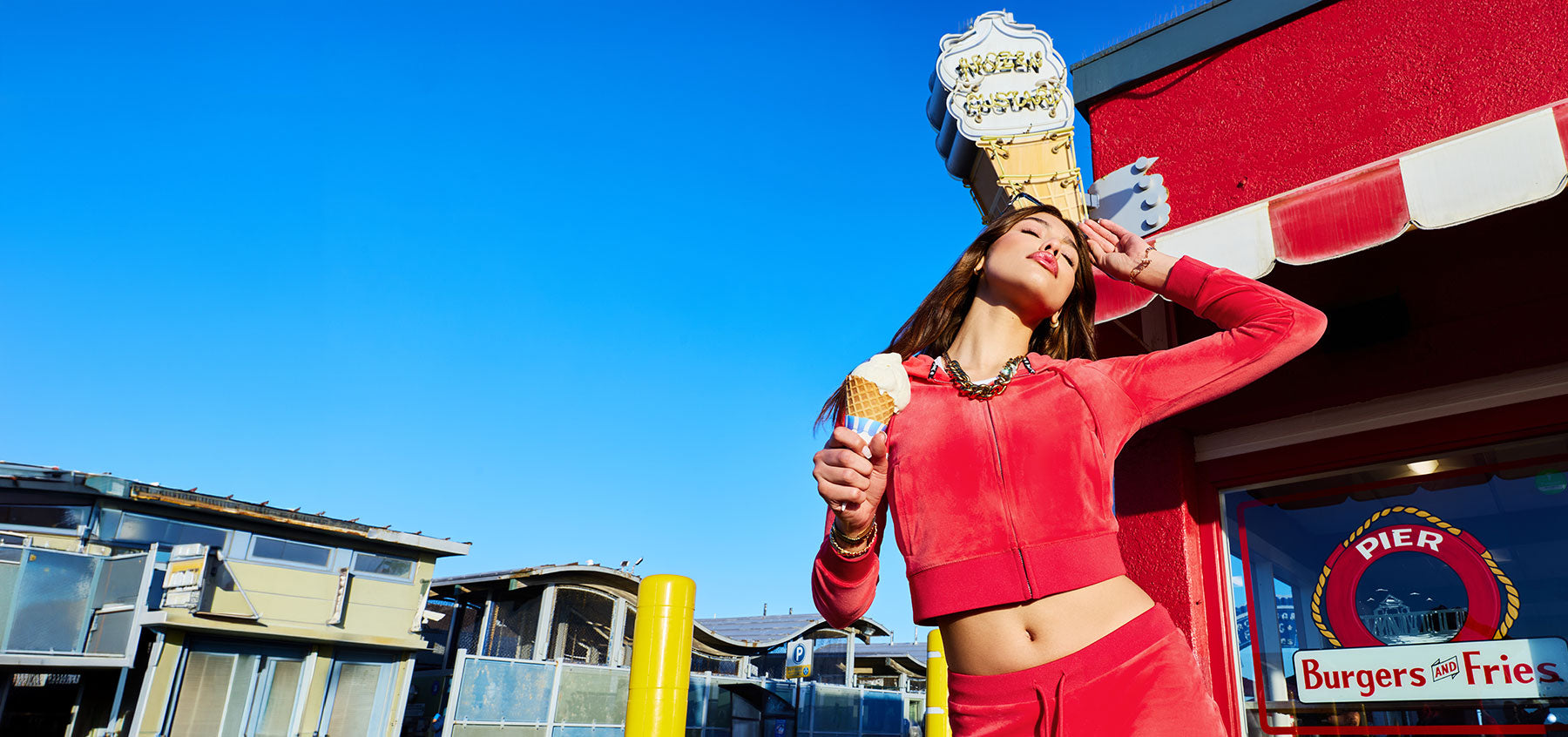 Person in red tracksuit standing on a pier holding ice cream