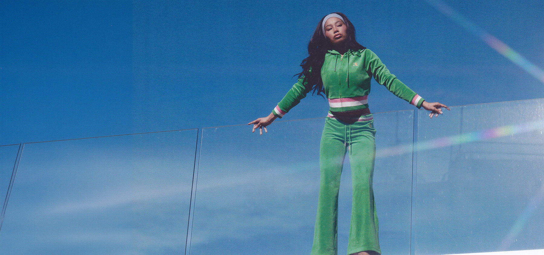 Woman in green tracksuit standing at the top of a building against a blue sky