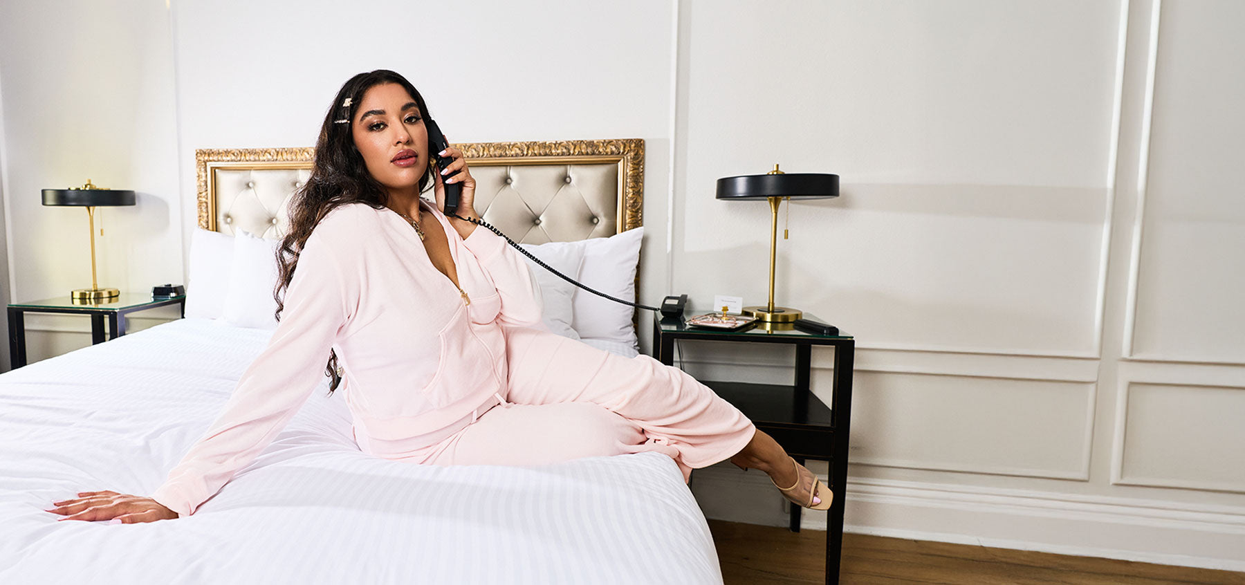 Woman in pink tracksuit sitting on a bed in a stylish bedroom.