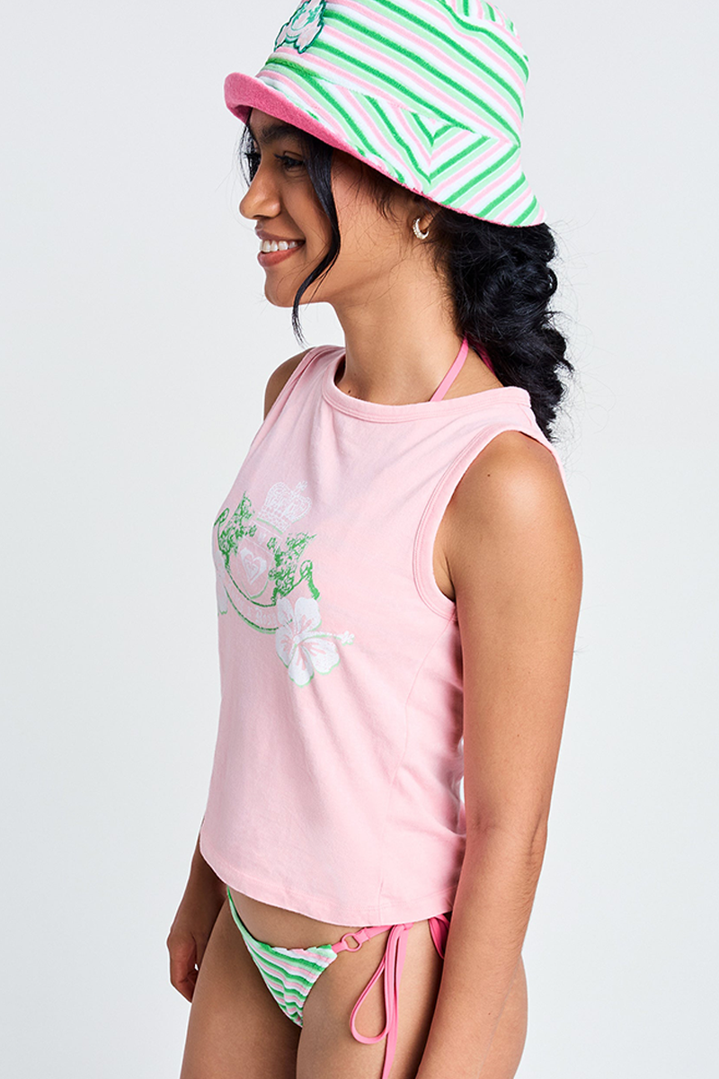 Smiling sideways, a person wears the Candy Pink Roxy x Juicy Crest Tank Top (100% cotton, floral print), paired with a pink and green striped bucket hat and matching bikini bottoms, all set against a plain white background.