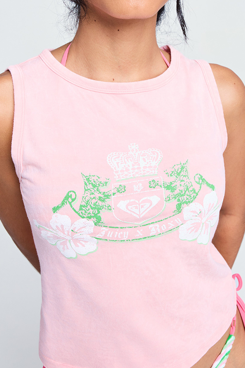 A person wears the Candy Pink Roxy x Juicy Crest Tank Top, a sleeveless 100% cotton top featuring a crown, shield, two cats, hibiscus flowers, and Juicy x Roxy text. The person's head is partially out of frame.