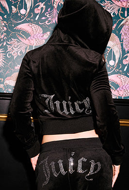 Person wearing a black hoodie and pants with 'Juicy' text, standing against a decorative wall.