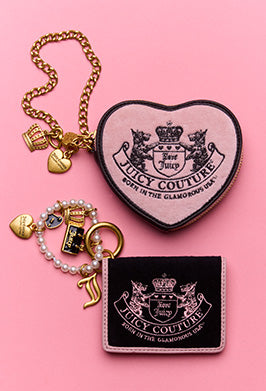 Juicy Couture heart-shaped pouch, keychain, and wallet on a pink background