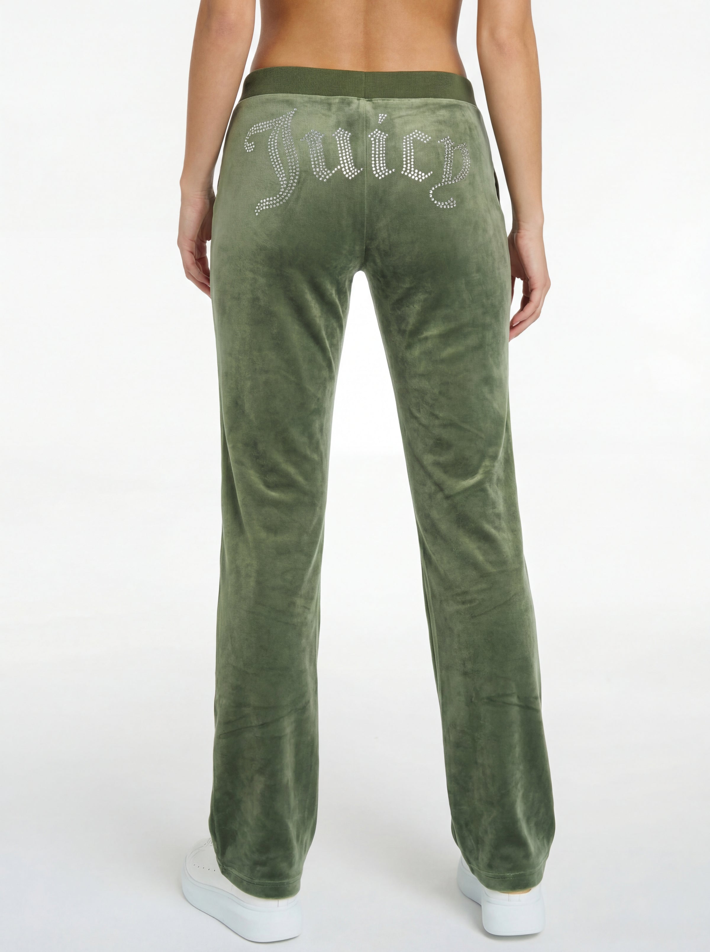 A person wearing OG Big Bling Velour Track Pants—REJUICED in green, featuring "Juicy" rhinestones on the back, stands against a white background. Only the lower back and legs are visible. Machine washable for easy care.