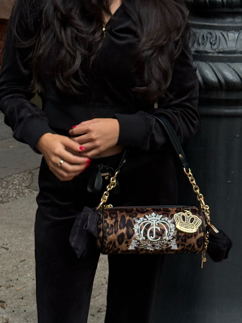 Crowns & Kisses Shoulder Bag: A cylindrical, leopard-print bag featuring an embroidered crest, gold-tone chain strap, a dangling crown charm, and a touch of feminine nostalgia.