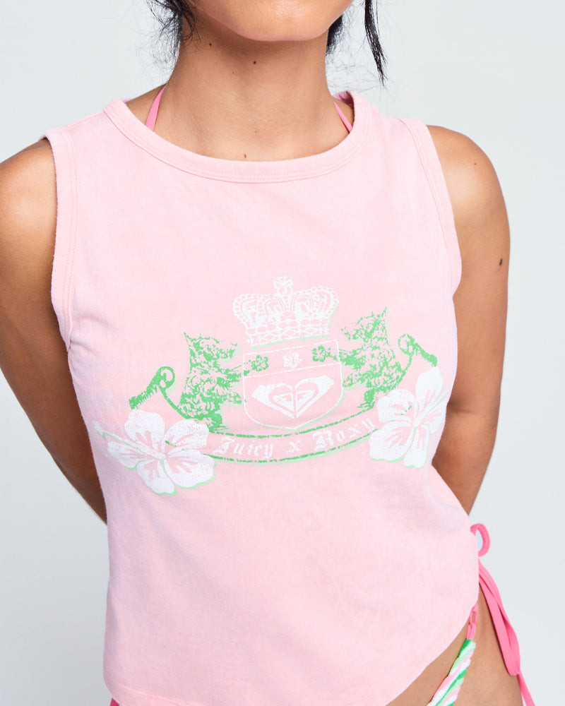 A person wears the Roxy x Juicy Crest Tank Top in candy pink, featuring floral accents, green and white crest graphics, and text. Their dark hair is loosely tied back, with only their upper body and part of a bikini bottom visible.