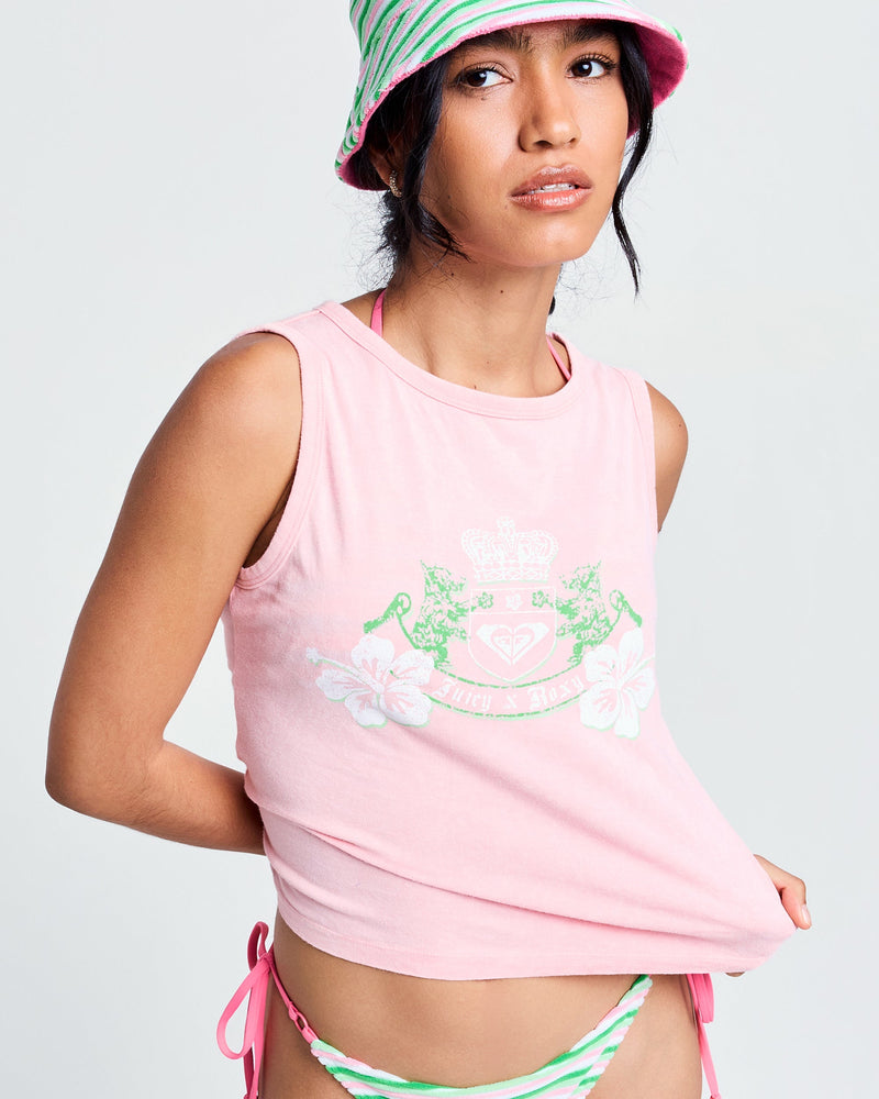 A woman wears the Roxy x Juicy Crest Tank Top in Candy Pink, featuring a white crest and 100% cotton fabric, paired with a pink and green striped bucket hat and matching bikini bottoms against a plain light background.