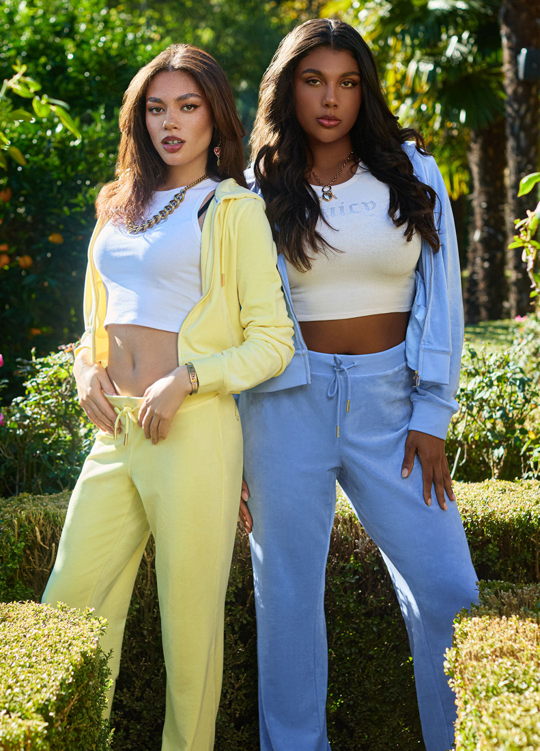 Two women in a pastel yellow tracksuit and a blue tracksuit together in a garden setting.
