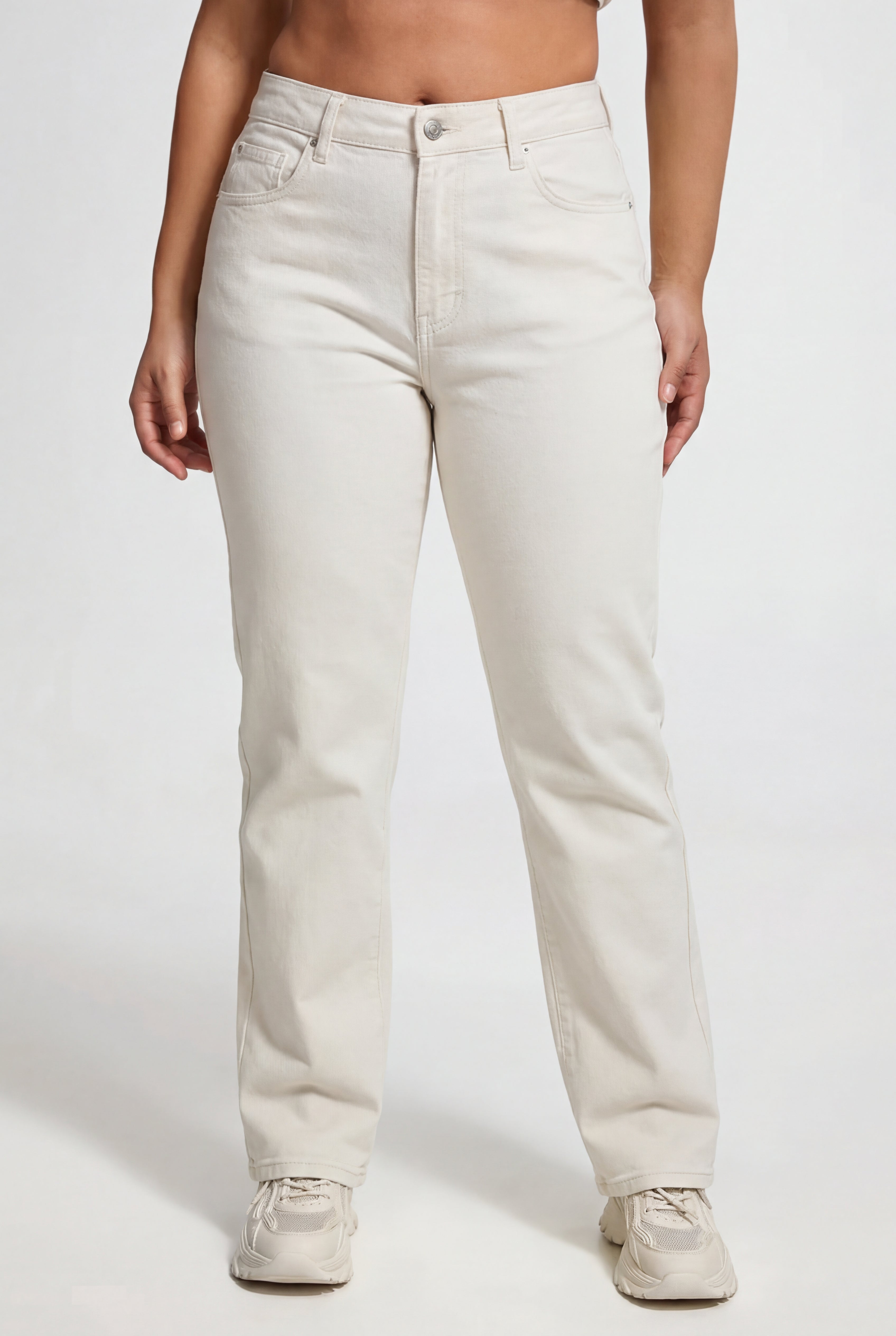 A person wearing White Denim Juicy Couture Jeans—REJUICED, featuring a high-waisted, straight-leg fit with pockets in light beige, paired with white athletic shoes, stands against a plain white background.