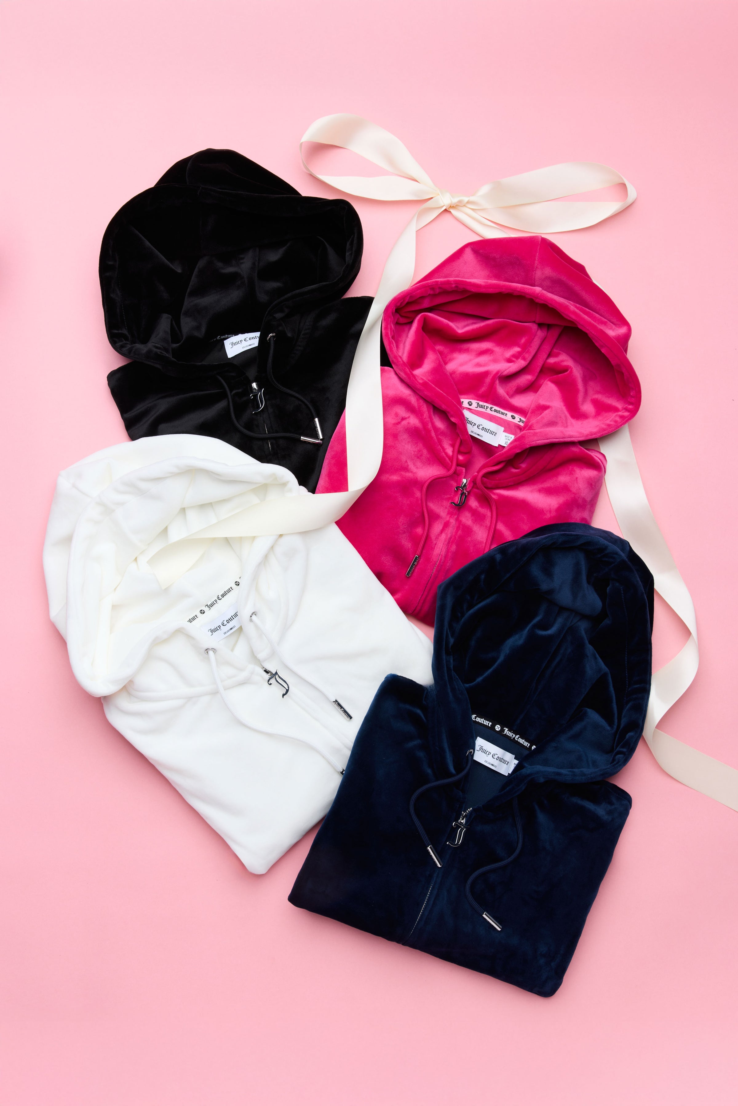 Four Juicy Couture hoodies in black, pink, white, and navy on a pink background