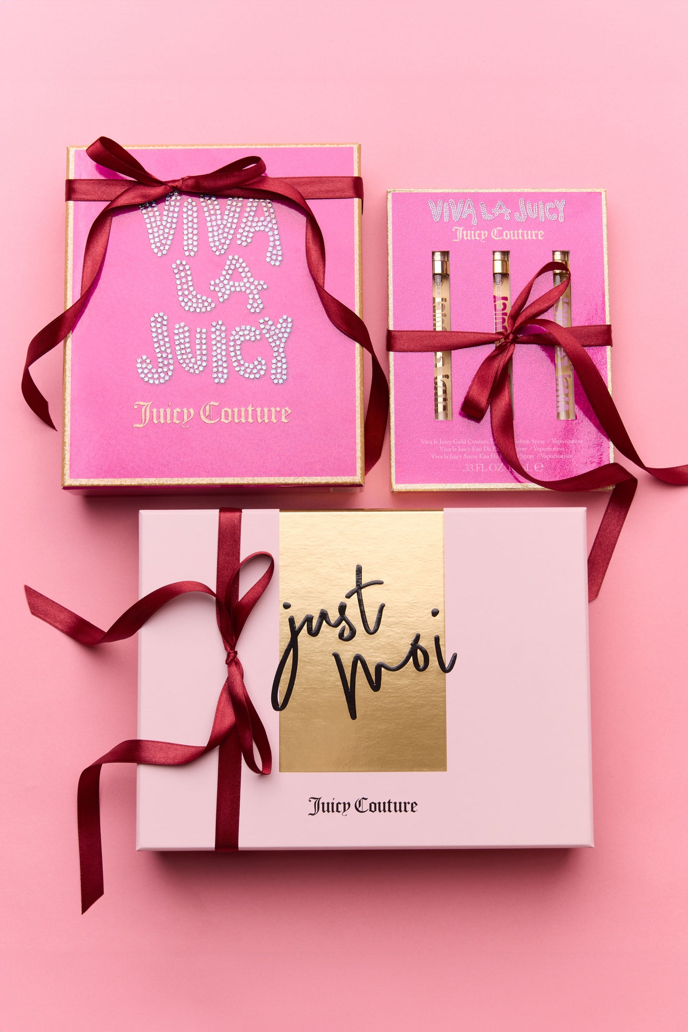 Juicy Couture perfume gift set including Viva La Juicy and Just Moi with pink boxes and red ribbons on a pink background