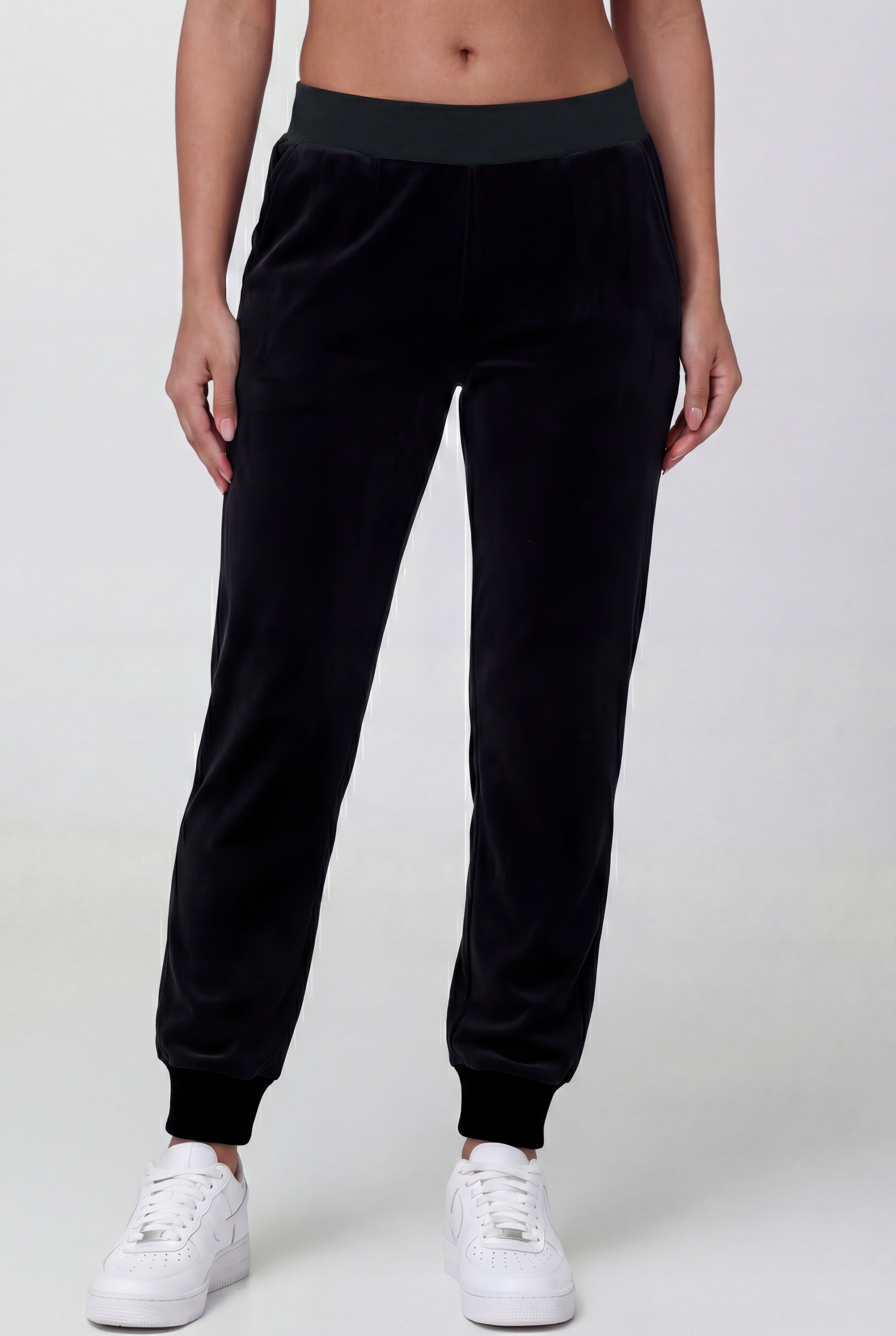 Someone wearing Black Velour Cinched Jogger Pants—REJUICED, featuring a dark waistband and cuffs, paired with white sneakers, stands against a plain light background.
