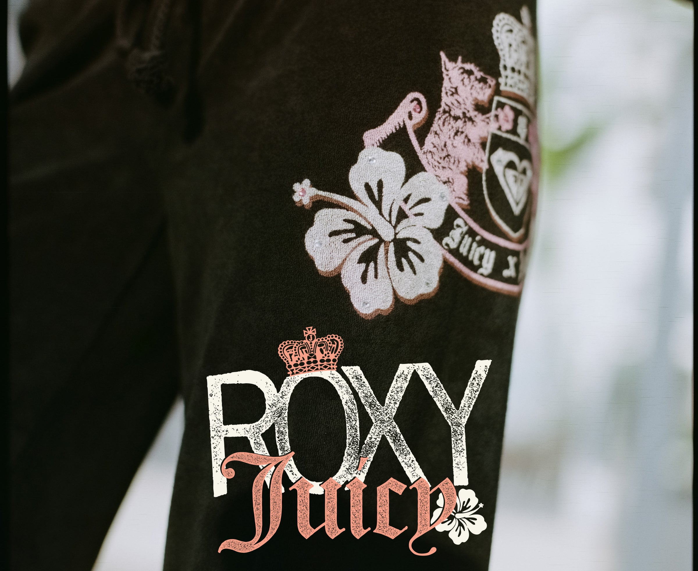 Black track pants with 'Roxy Juicy' branding and floral design on a blurred background